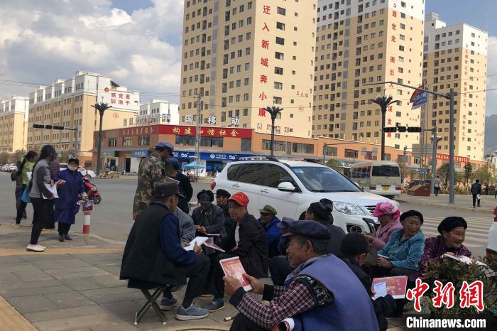 图为会泽县城易地扶贫搬迁安置点内，老人们聚在广场上聊天，身后是他们的新家。　缪超 摄