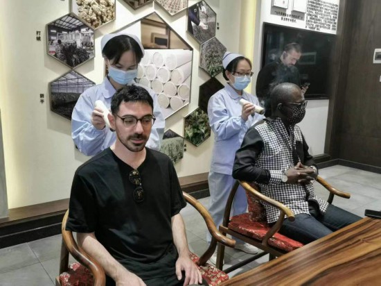 2023“一带一路”媒体合作论坛联合采访团团员在九牛草展示馆体验艾灸。(本报记者 黄超摄)