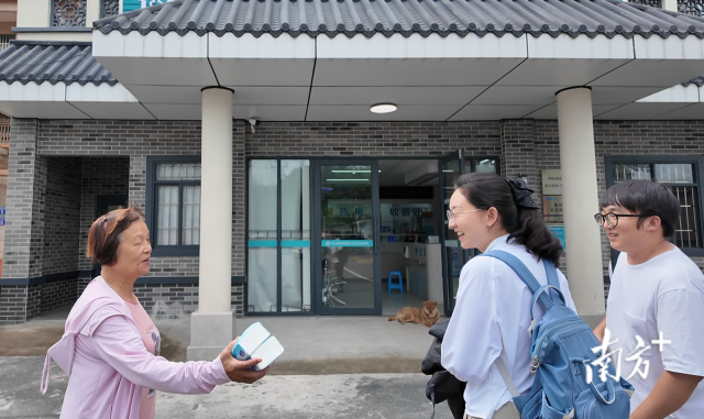 公共服务组成员王樱洁（中）和张龙（右）在崖口村卫生室前跟村民打招呼。